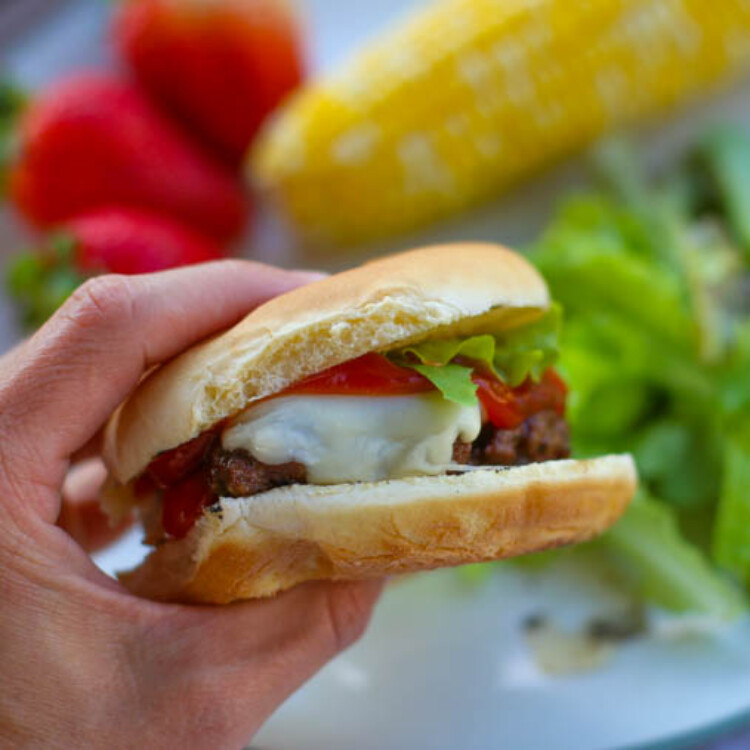 A hand holding a pesto burger with cheese, ketchup, and lettuce.