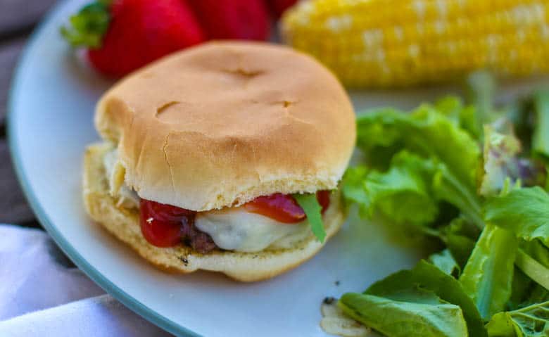 A pesto burger on a plate with salad, strawberries, and corn on the cob.