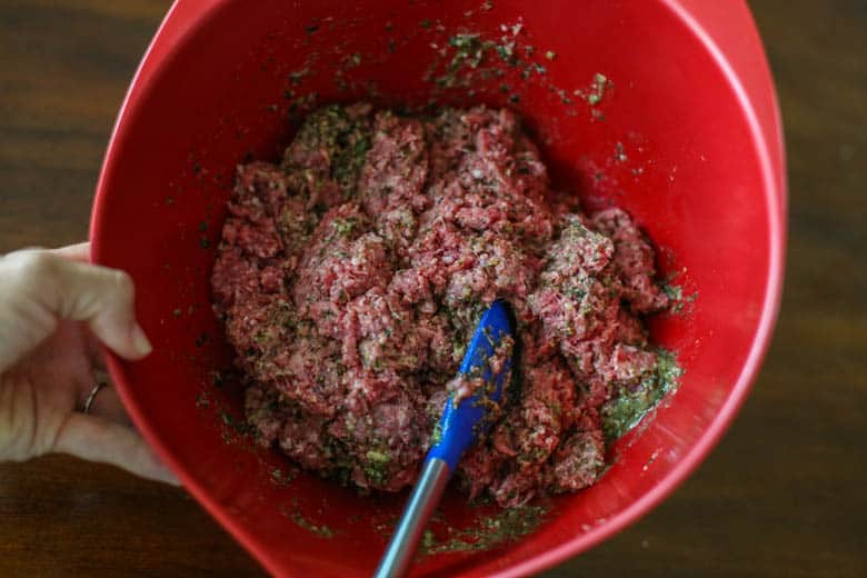 Ground beef being mixed with pesto for burgers.