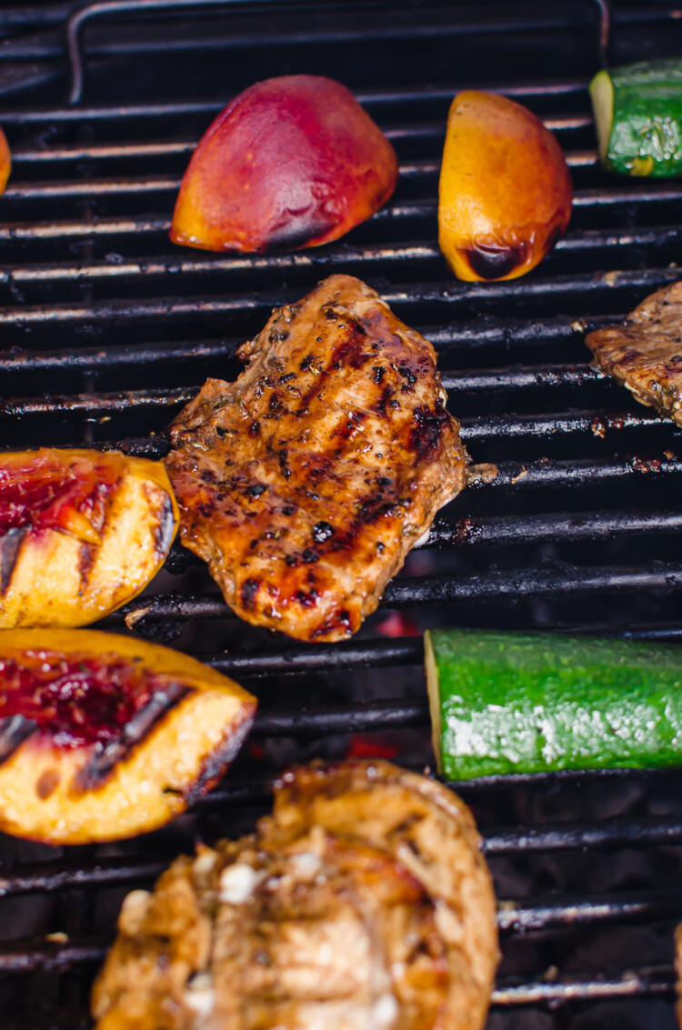 Grilled balsamic herb chicken on the grill with zucchini and peaches also being grilled.