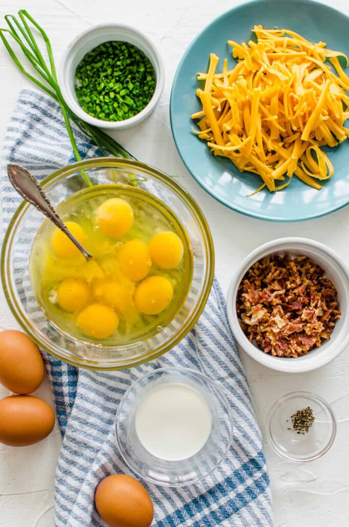 ingredients in bowls like eggs, cheese, bacon, milk, and chives