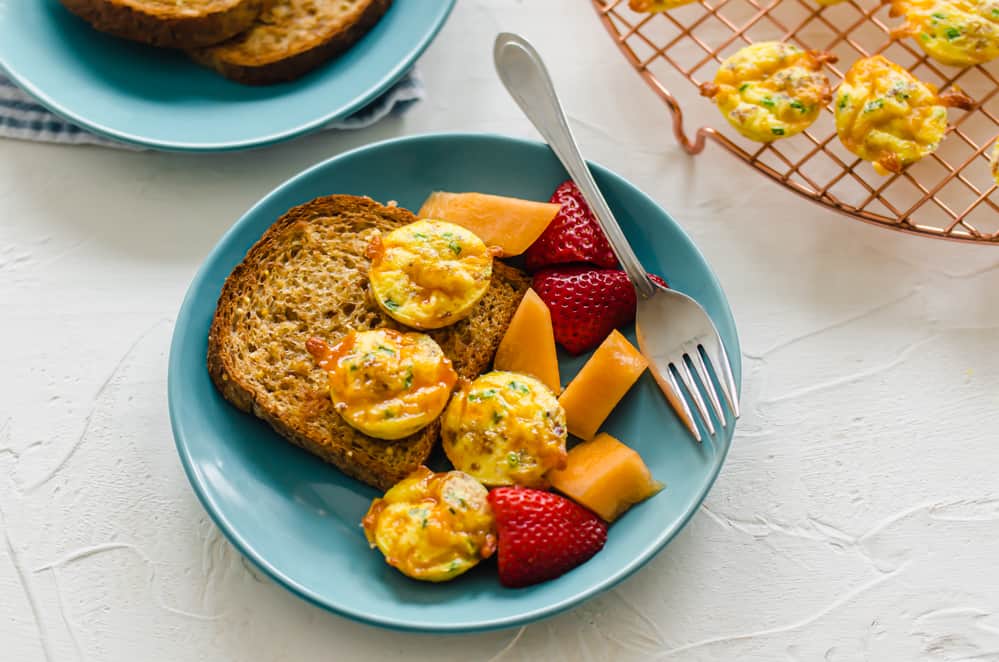 mini egg muffins on a blue plate with whole grain toast and fresh cut up cantaloupe and strawberries