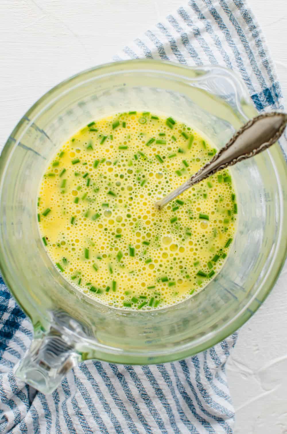 Beaten eggs in a glass mixing bowl with chives.