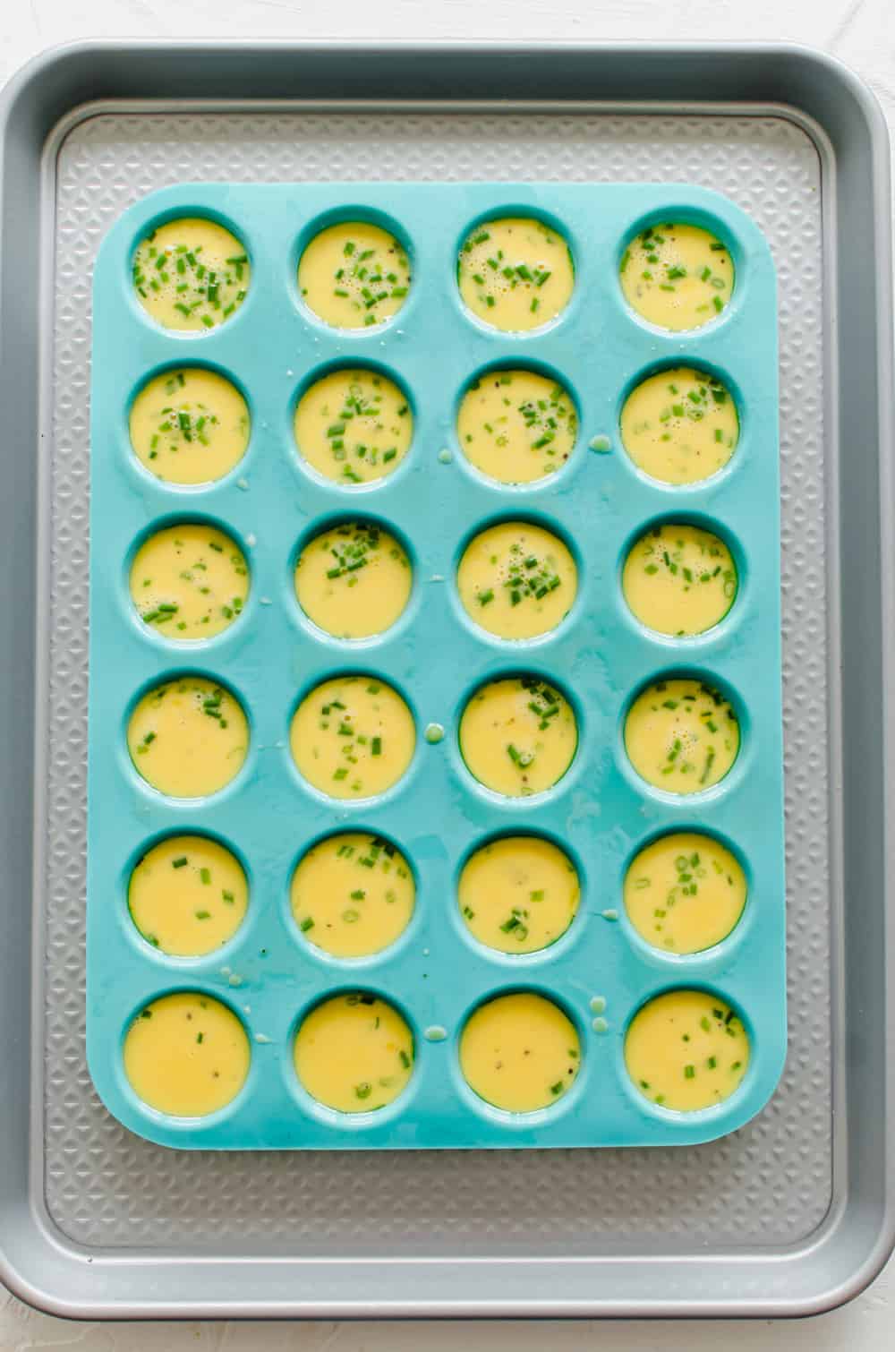 Beaten eggs with chopped chives in a silicone mini muffin tin ready to bake.