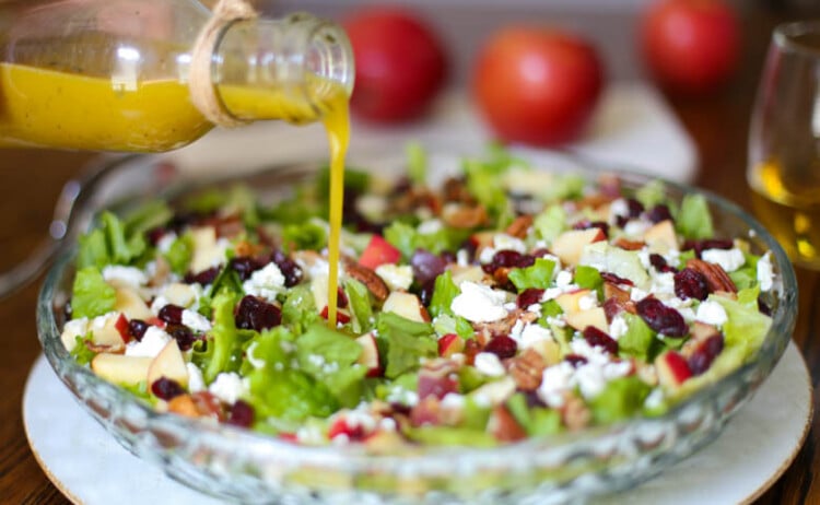 Autumn Salad in a glass bowl with Apple Cider Vinaigrette being poured on top.