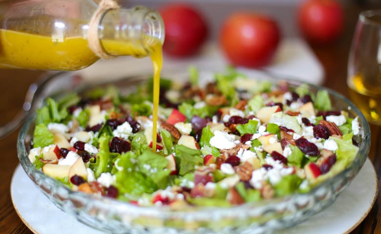 autumn chopped salad in a serving platter with apple cider vinaigrette being drizzled over the top