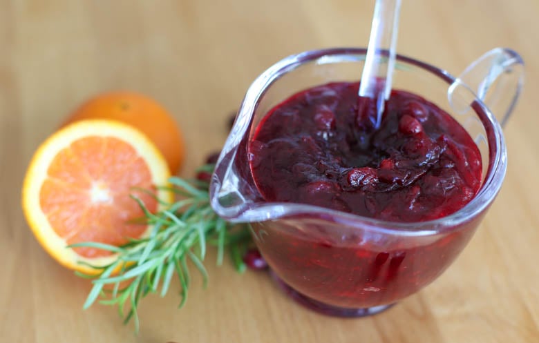 homemade cranberry sauce in a glass bowl with orange and rosemary as garnish