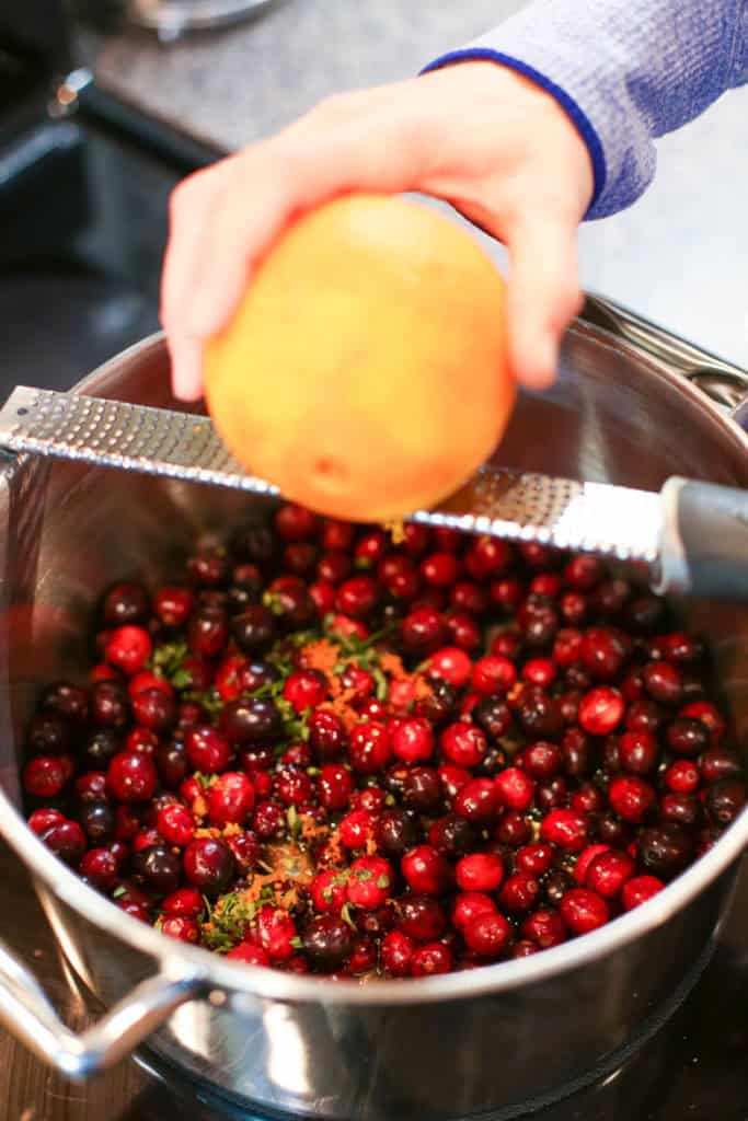 zesting orange over homemade cranberry sauce in a pot