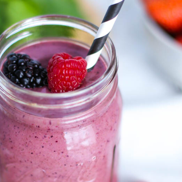 Very berry smoothie in a mason jar with a straw, as well as a blackberry and raspberry on top.
