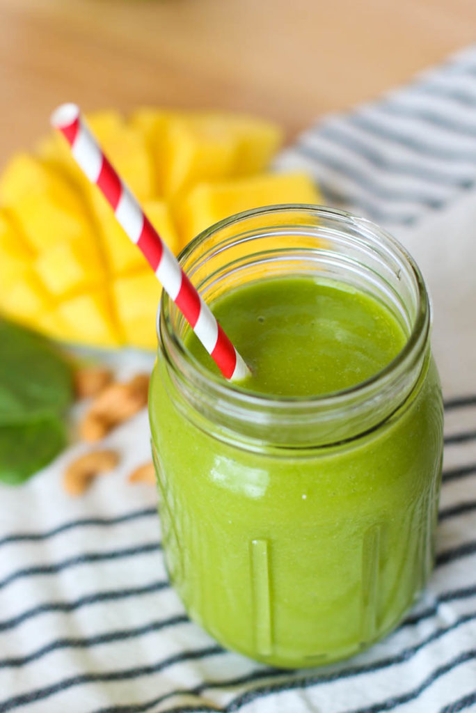 Tropical smoothie recipe in a mason jar with mango in the background 
