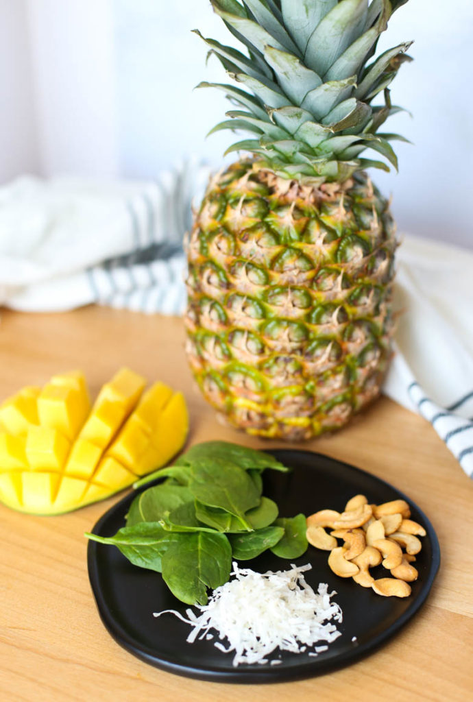 Ingredients for a tropical smoothie recipe: pineapple, mango, spinach, cashews on cutting board