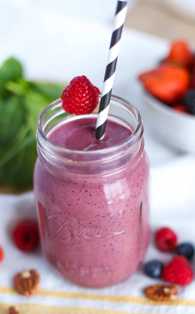 Berry smoothie in mason jar with a raspberry on top and a black and white striped straw in it.