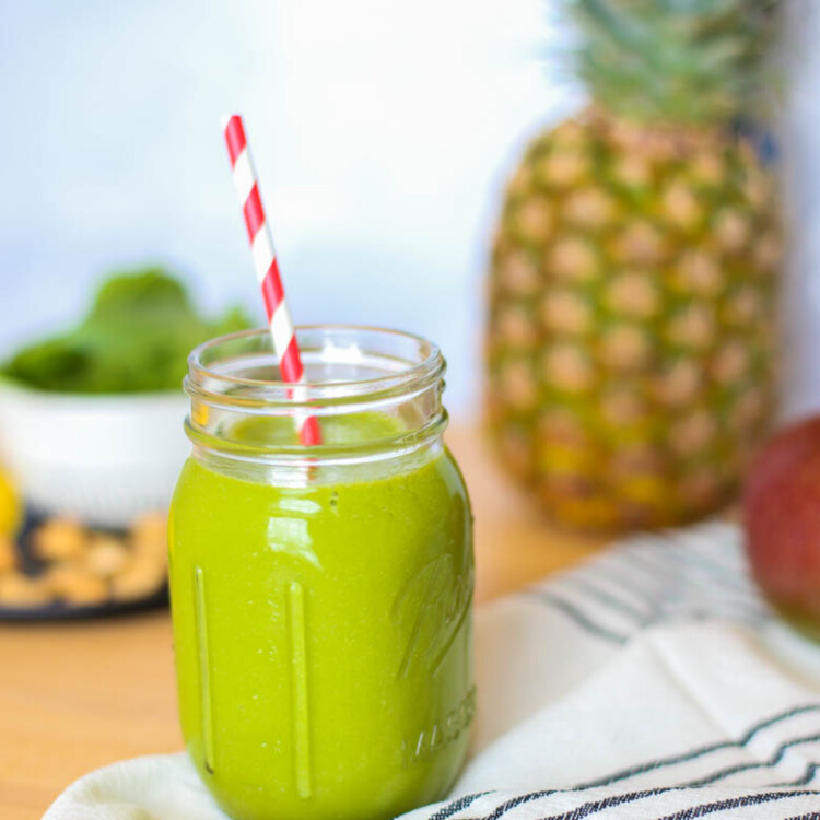 Tropical green smoothie in a mason jar with a straw and a whole pineapple in the background.