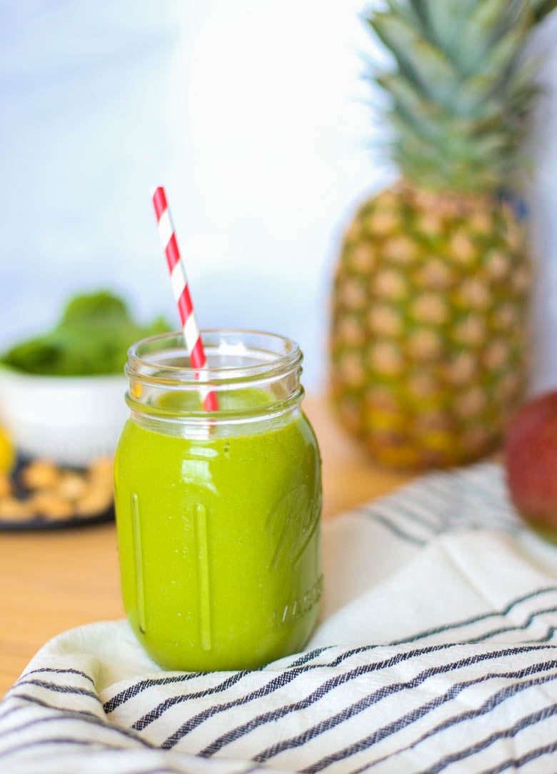 Tropical green smoothie in a mason jar with a straw and a whole pineapple in the background.