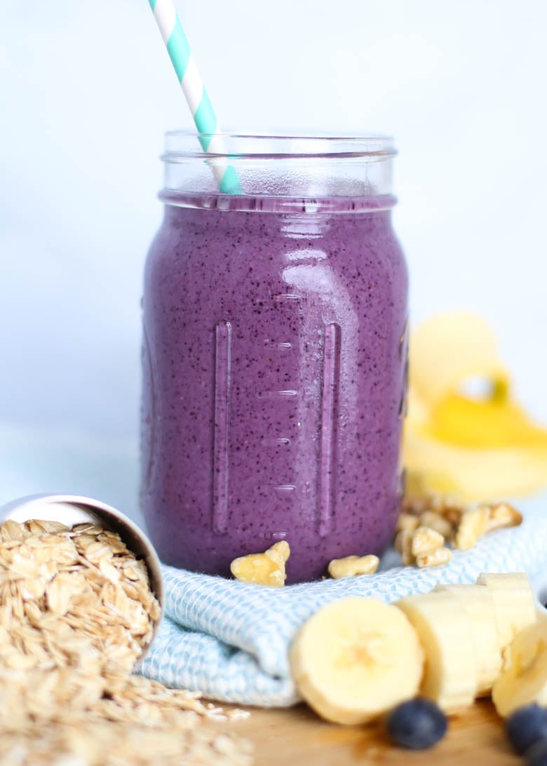 Blueberry muffin smoothie in mason jar with straw with a measuring cup of oats, chopped walnuts and banana slices around it.