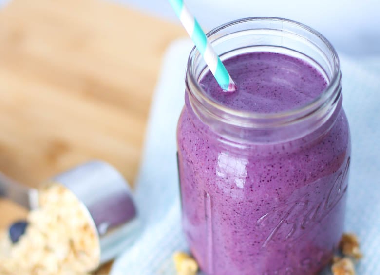 Blueberry smoothie in a mason jar with and a measuring cup of oats in the background.