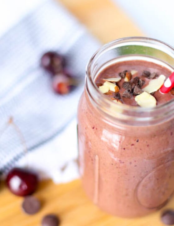 Chocolate covered cherry smoothie in a mason jar with dark sweet cherries scattered around it.