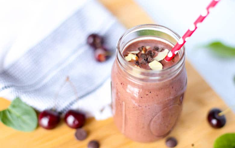 Chocolate covered cherry smoothie in a mason jar with dark sweet cherries scattered around it.