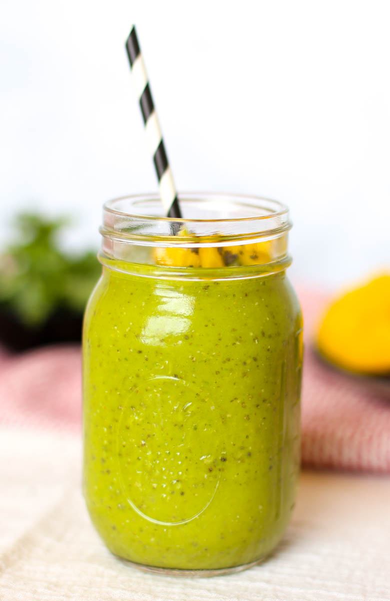 Green machine smoothie in mason jar with straw and mango chunks and chia seeds on top.