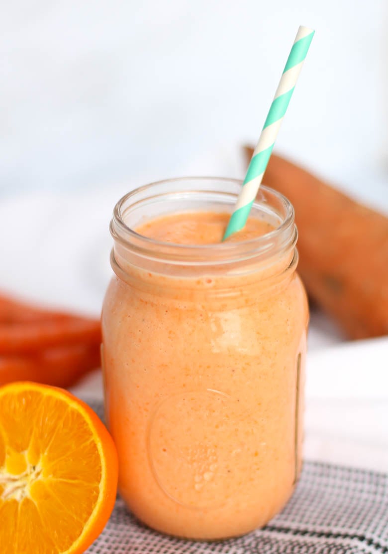 Orange smoothie in a mason jar with a whole sweet potato in the background and half an orange sitting next to it.