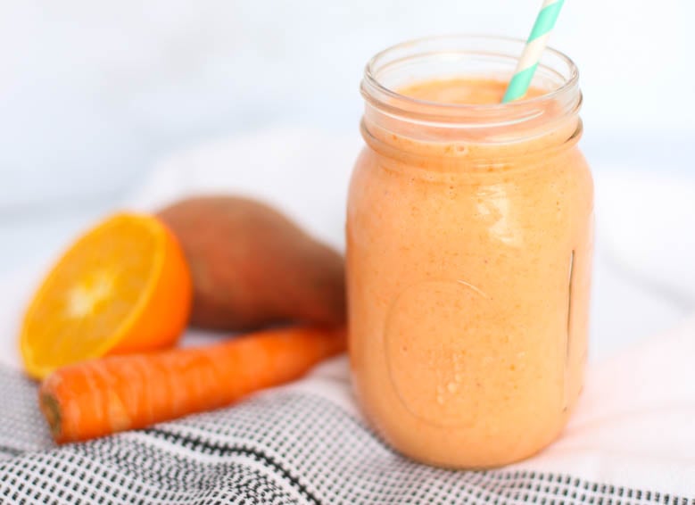 Orangesicle smoothie in a mason jar with a straw and a carrot, sweet potato, and half an orange sitting next to it.