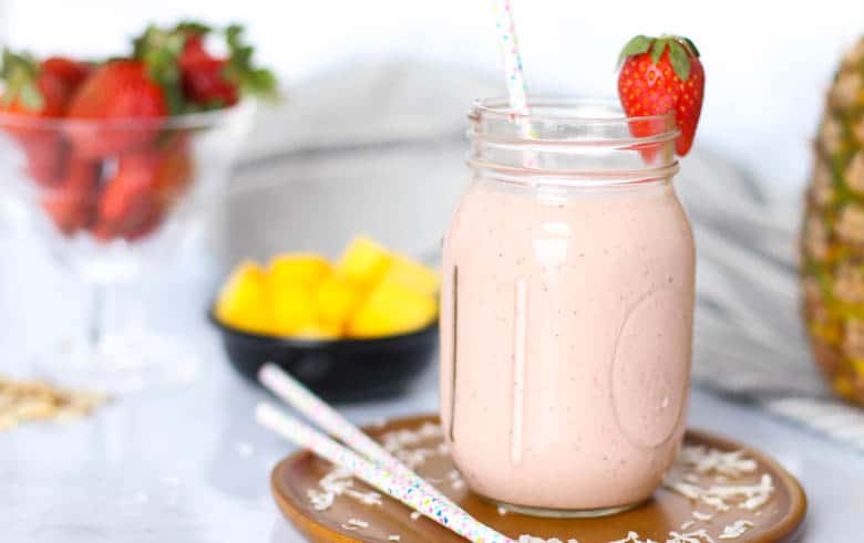 Pina colada smoothie in a mason jar with ingredients in the background.