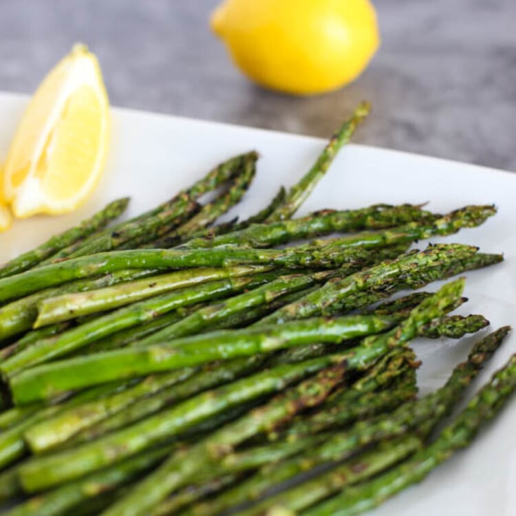 Roasted asparagus on a white plate with lemon wedges.