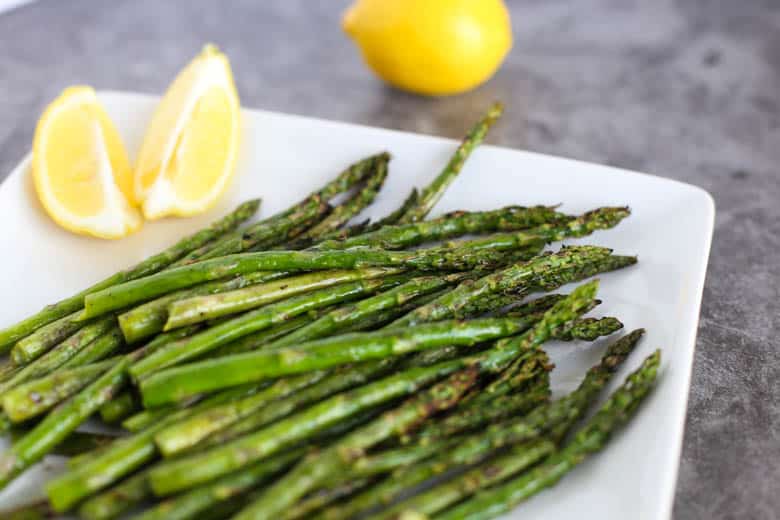 Grilled asparagus on a white plate with lemons