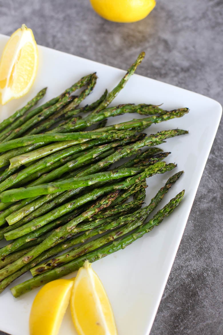 Grilled asparagus on a white plate with lemon wedges.