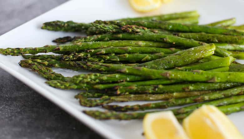 Roasted asparagus on a serving platter with lemon wedges on the side.