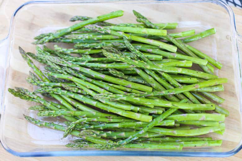 Seasoned fresh asparagus stalks in a a baking dish.