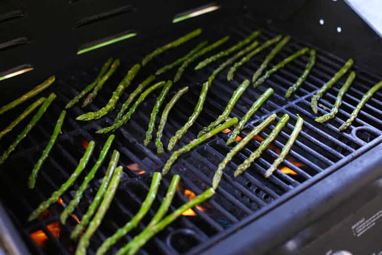 Asparagus on the grate of a grill with flames underneath.