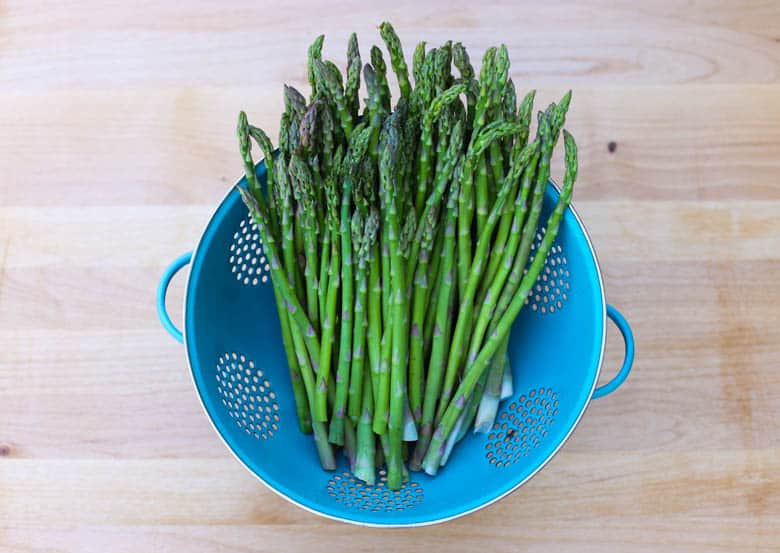 Fresh asparagus in a blue colander.