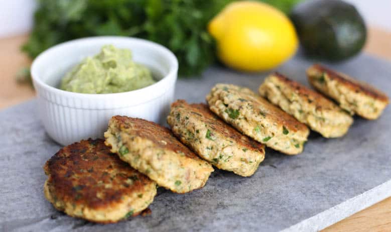 Salmon patties lined up to serve with lemony avocado sauce in a white bowl.