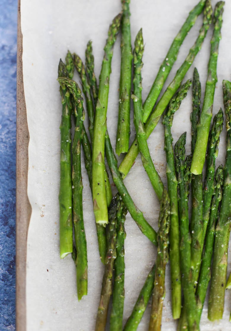 Oven roasted asparagus on a sheet pan sprinkled with salt and pepper.