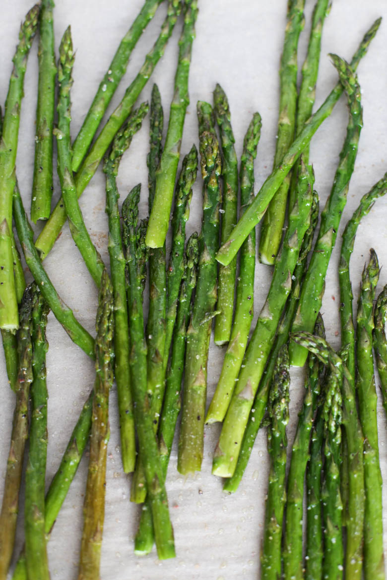 Oven roasted asparagus on a parchment paper-lined sheet pan.