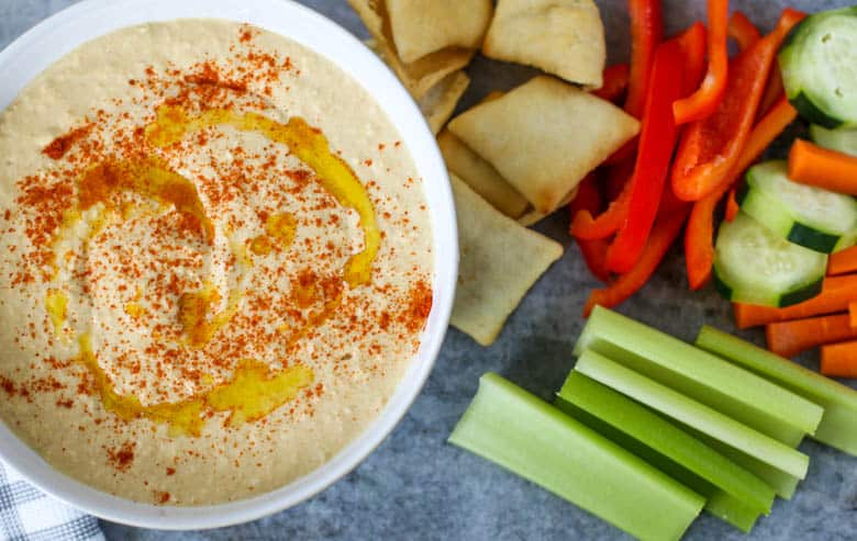 Blender hummus in a bowl with veggies and pita chips next to it.