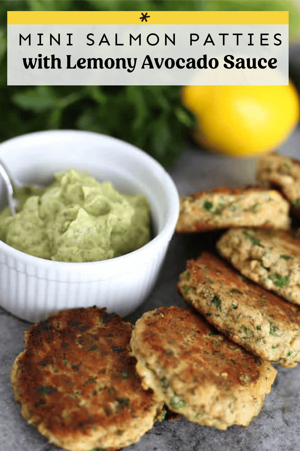 Salmon patties laid on a gray platter with a small bowl of lemony avocado sauce.