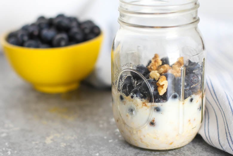 Blueberry muffin overnight oats in a mason jar with a yellow bowl of blueberries in the background.