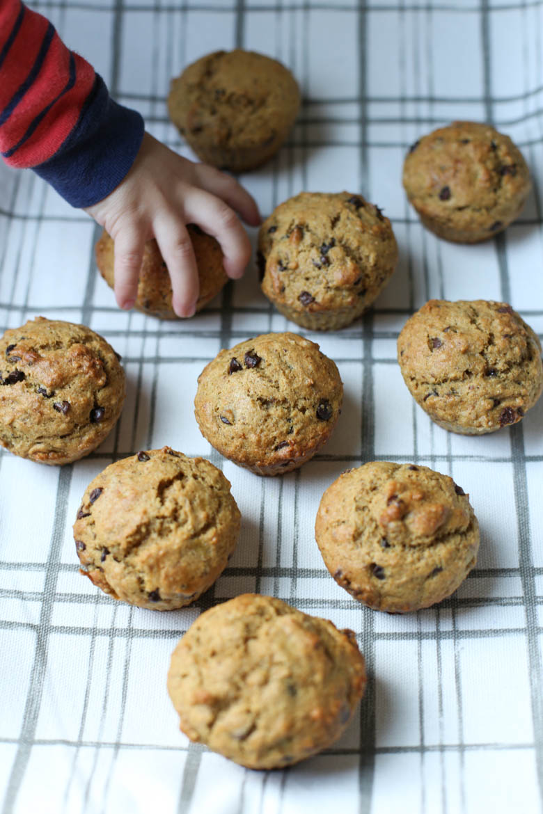 Chocolate chip banana muffins on a tea towel with child's hand reaching for one muffin.