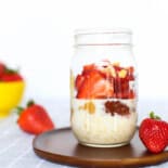 Mason jar or peanut butter and jelly overnight oats sitting on a wooden platter on the counter.