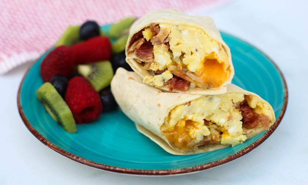 freezer breakfast burrito sliced in half and stacked on a teal plate with berries on the side