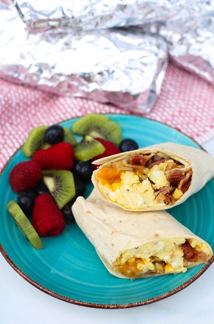 Breakfast burrito cut in half on a plate with fresh fruit.