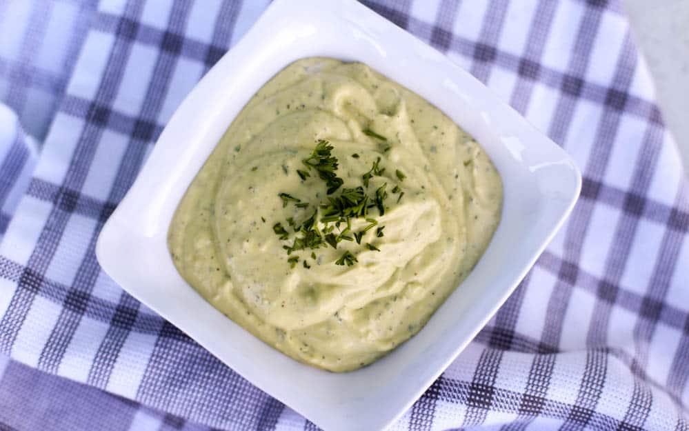 Homemade avocado aioli in a white square dish with minced parsley sprinkling on top.