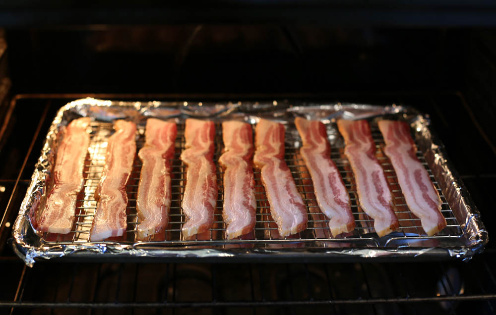 cooking bacon slices in the oven on a rimmed baking sheet 