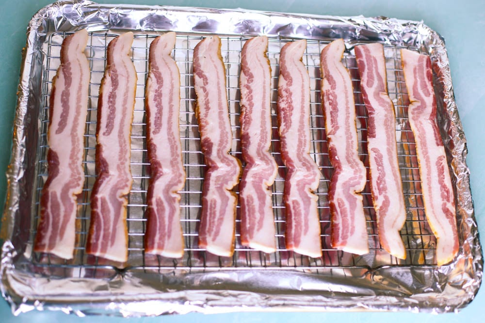 uncooked bacon lined up on a baking rack