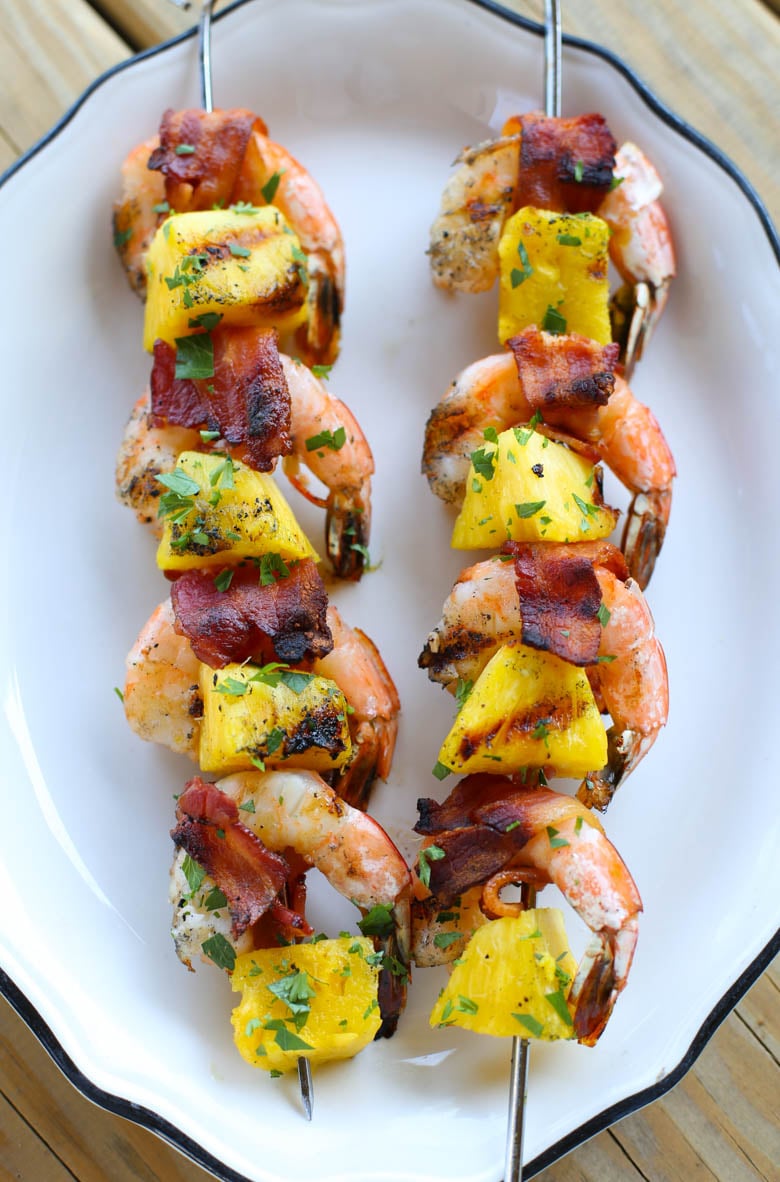 Two grilled bacon-wrapped shrimp kabobs on a white platter.