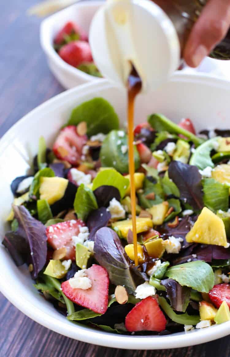 Strawberry avacado in a white bowl with honey balsamic dressing being poured on it.