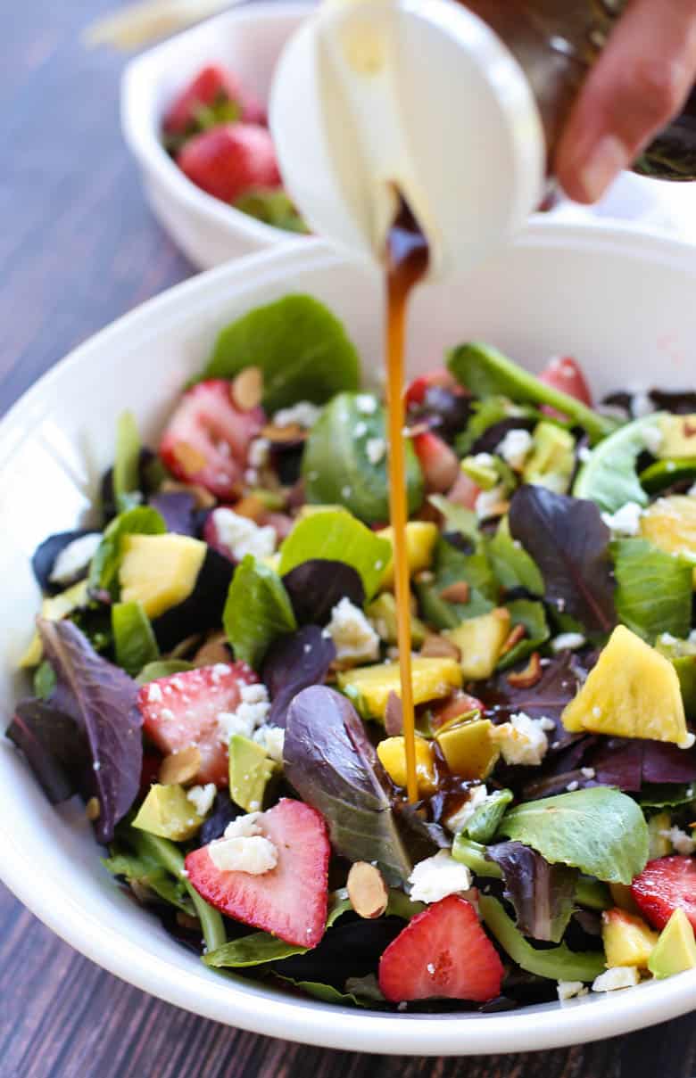 Strawberry chicken salad with honey balsamic dressing being poured over it. 