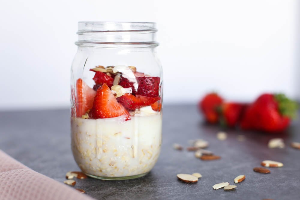 Strawberry shortcake overnight oats in a mason jar sitting on a table with whole strawberries in the background and sliced almonds scattered on the table.